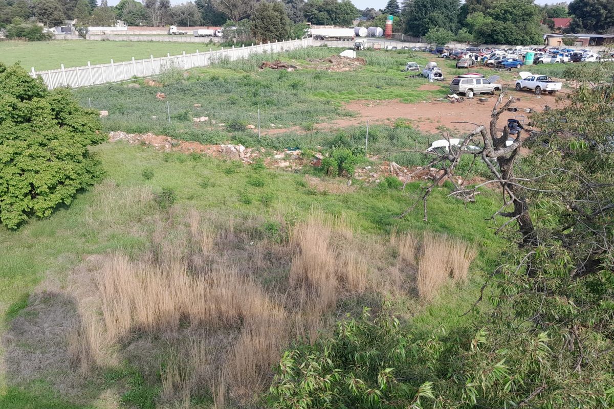 Aerial view of a large, undeveloped plot of land featuring perimeter fencing and boundary walls, currently showing signs of neglect and overgrown vegetation.