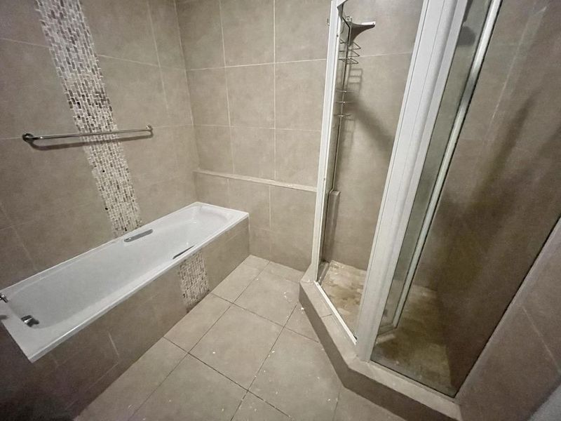 A functional bathroom featuring a built-in bathtub, separate shower enclosure, and neutral floor-to-ceiling tiling with a decorative mosaic accent strip.