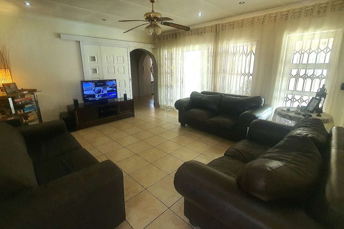 Spacious living room featuring tiled flooring, a ceiling fan, and large windows with security gates, providing access to the outdoor area.