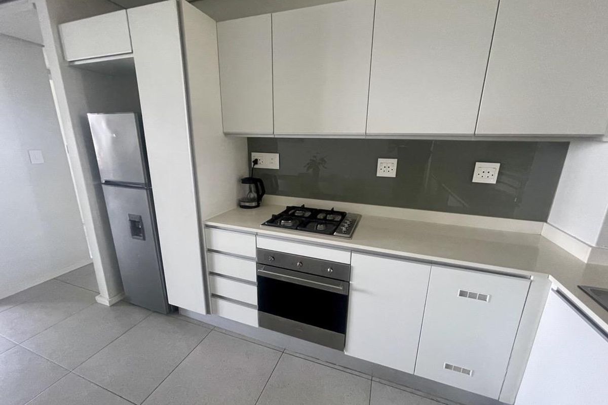 Modern kitchen featuring sleek white cabinetry, stone countertops, a built-in gas hob, oven, and a glass splashback in a contemporary apartment setting.