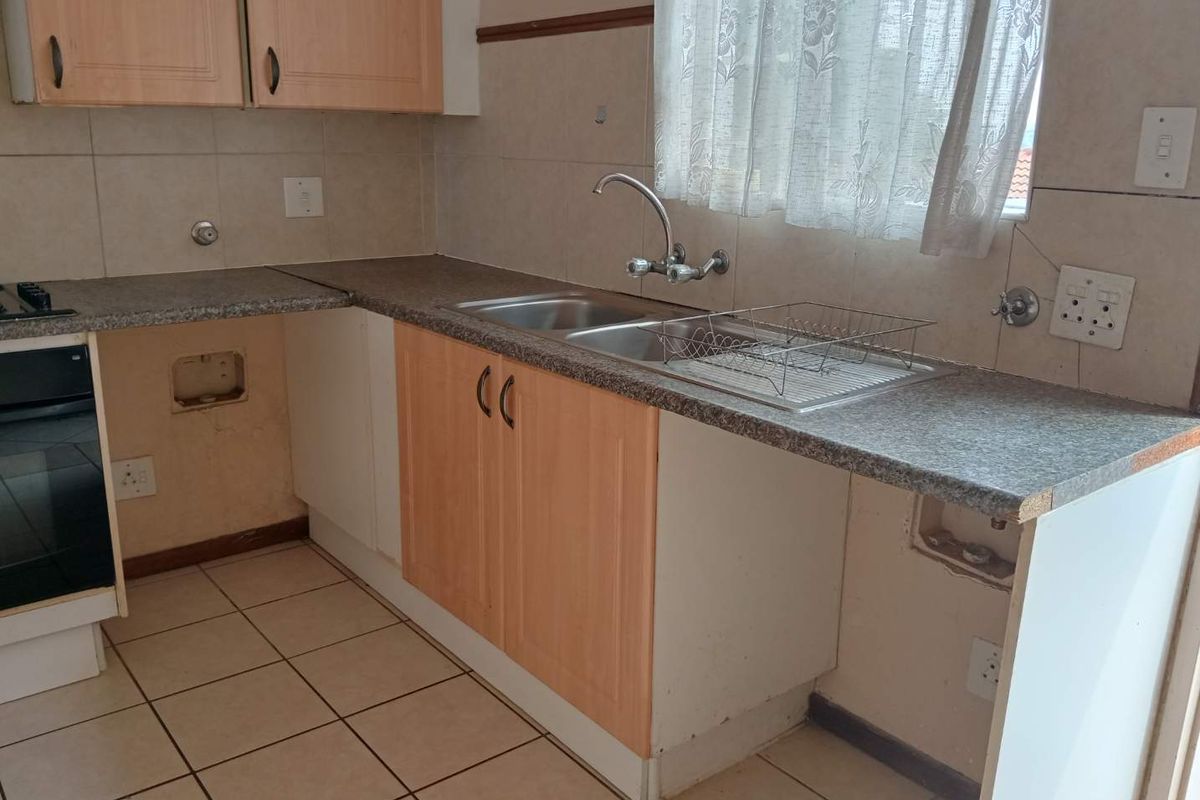 A dated kitchen featuring laminate cabinetry, a stainless steel double sink, and ceramic tiling, currently requiring cosmetic updates and repairs to built-in fixtures.