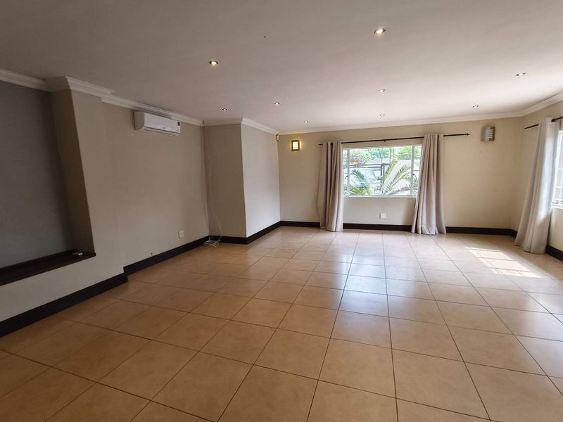 A spacious, empty living room featuring neutral tiled flooring, recessed downlighting, and a wall-mounted air conditioning unit.