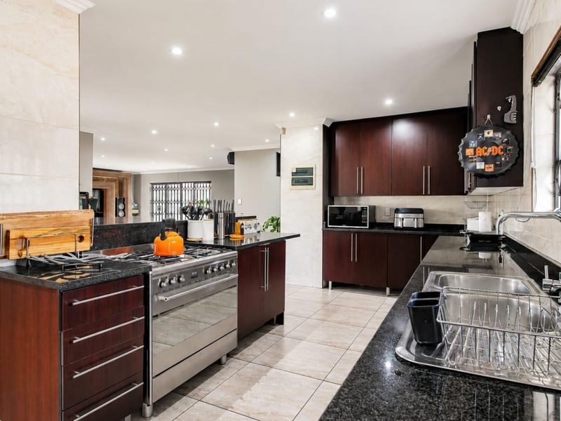 Spacious kitchen featuring dark wood cabinetry, granite countertops, a stainless steel gas stove, and double basin sink, with open flow to the living area.