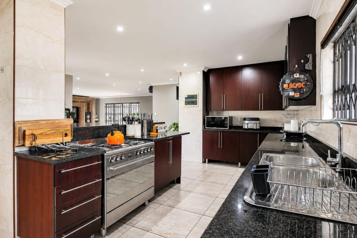 Spacious kitchen featuring dark wood cabinetry, granite countertops, a stainless steel gas stove, and double basin sink, with open flow to the living area.