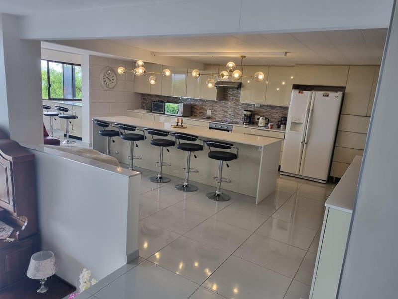 Spacious open-plan kitchen featuring a large central island, modern cabinetry, mosaic backsplash, and sleek tiled flooring, perfect for casual dining and entertaining.