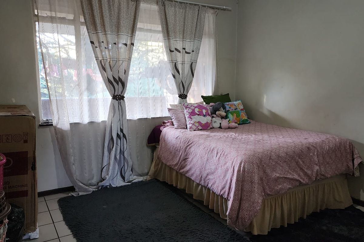 A bedroom featuring tiled flooring and a large window with curtain tracks, providing natural light to the space.