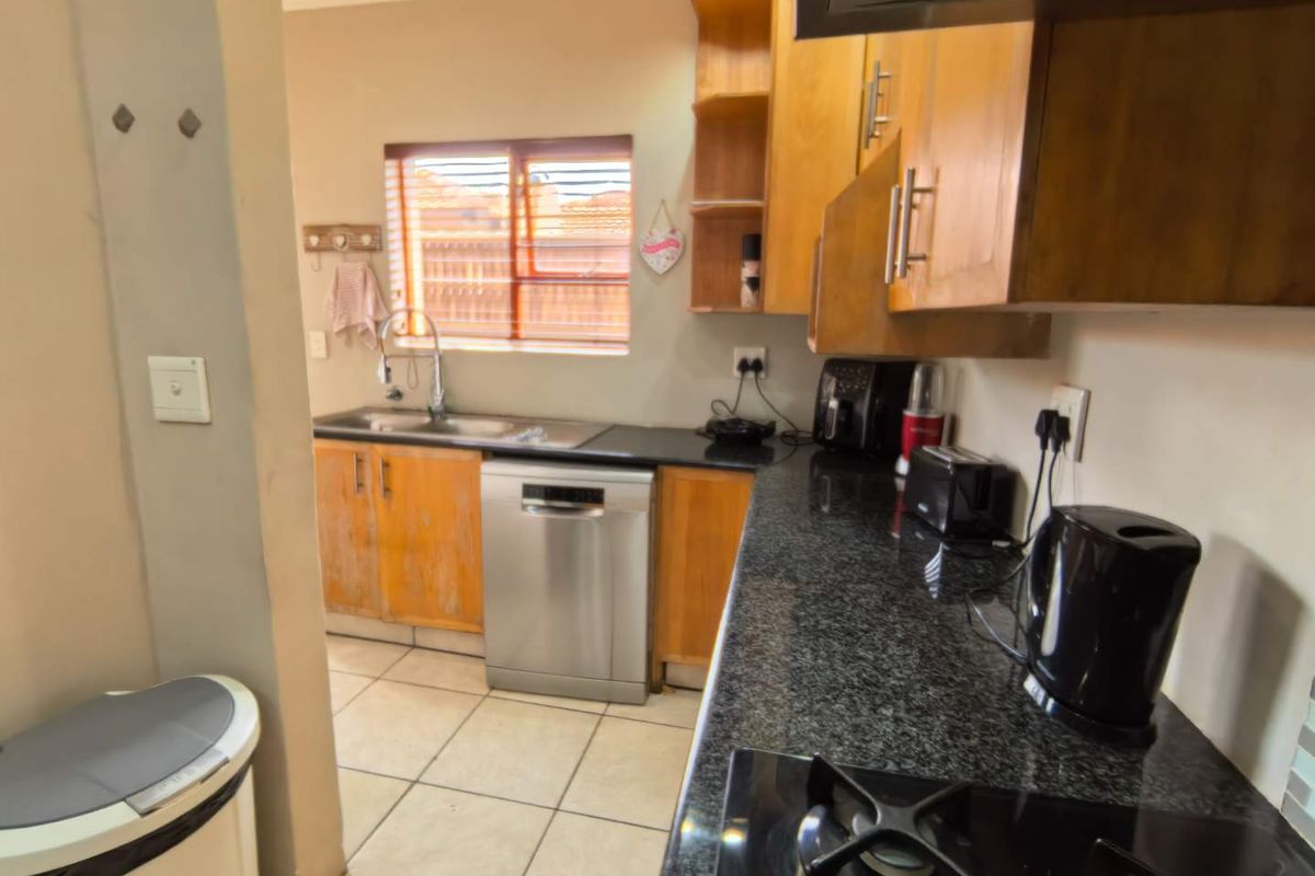 Functional kitchen featuring granite countertops, wooden cabinetry, tiled flooring, and a built-in gas hob with extractor fan.