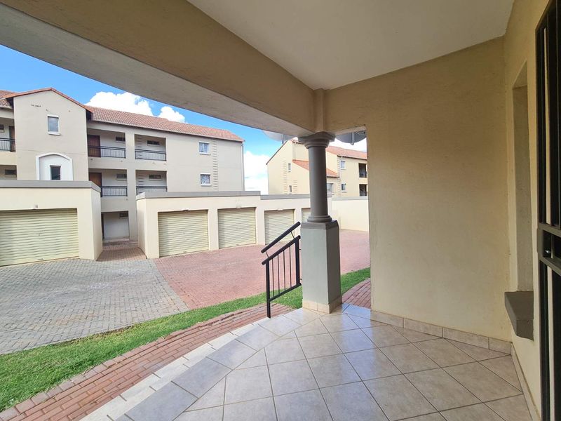 A covered patio area with tiled flooring, overlooking a paved complex driveway with multiple garage units.