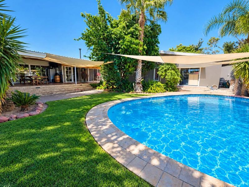 A well-maintained outdoor entertainment area featuring a circular swimming pool, paved surround, lush garden, and shaded patio space perfect for relaxation.