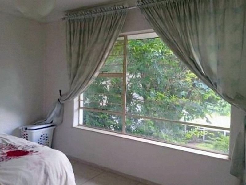 A bedroom featuring a large window with natural light and tiled flooring, offering a view of the surrounding greenery.