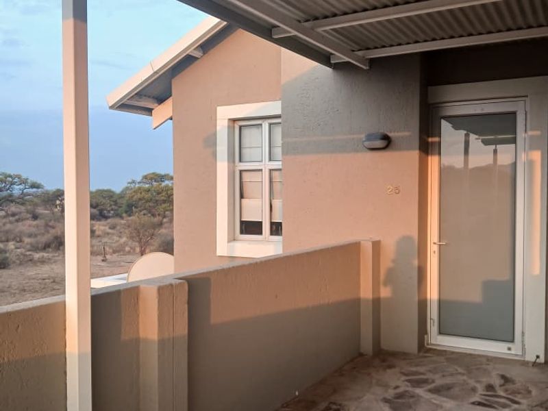 A covered patio area featuring stone flooring, a corrugated metal roof, and a glass panel entrance door with views of the surrounding landscape.