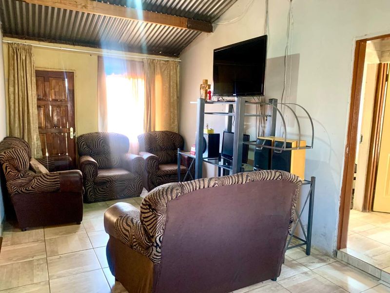 A living room featuring tiled flooring and an exposed corrugated metal ceiling, providing a basic, functional space with potential for cosmetic updates.