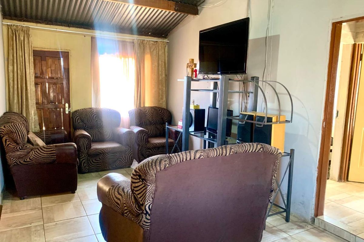 A living room featuring tiled flooring and an exposed corrugated metal ceiling, providing a basic, functional space with potential for cosmetic updates.