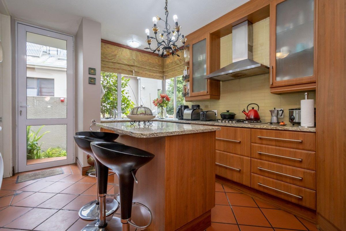 A functional kitchen featuring wooden cabinetry, granite countertops, a central island, and a stainless steel extractor fan, with direct access to the outdoor area.