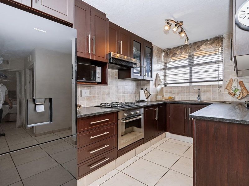 A well-maintained kitchen featuring dark wood cabinetry, granite countertops, built-in oven, gas hob, and tiled finishes throughout.