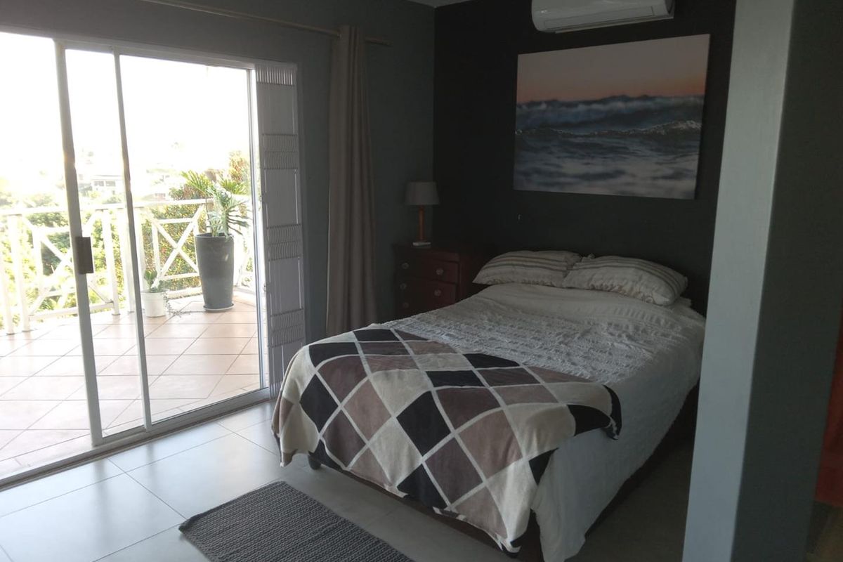 A well-maintained bedroom featuring tiled flooring, a split-system air conditioner, and large sliding glass doors providing direct access to an outdoor balcony.