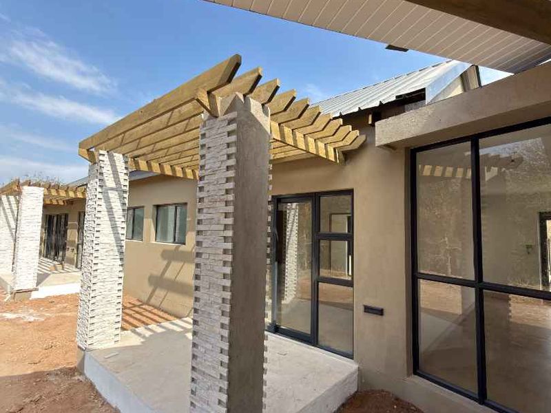 A modern covered patio featuring a timber pergola, stone-clad pillars, and large aluminium sliding doors, currently awaiting final landscaping and ground finishing.