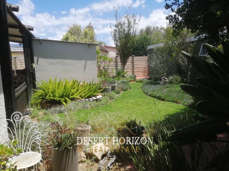 A well-maintained rear garden featuring a lush lawn, landscaped garden beds, and secure precast concrete boundary walls.