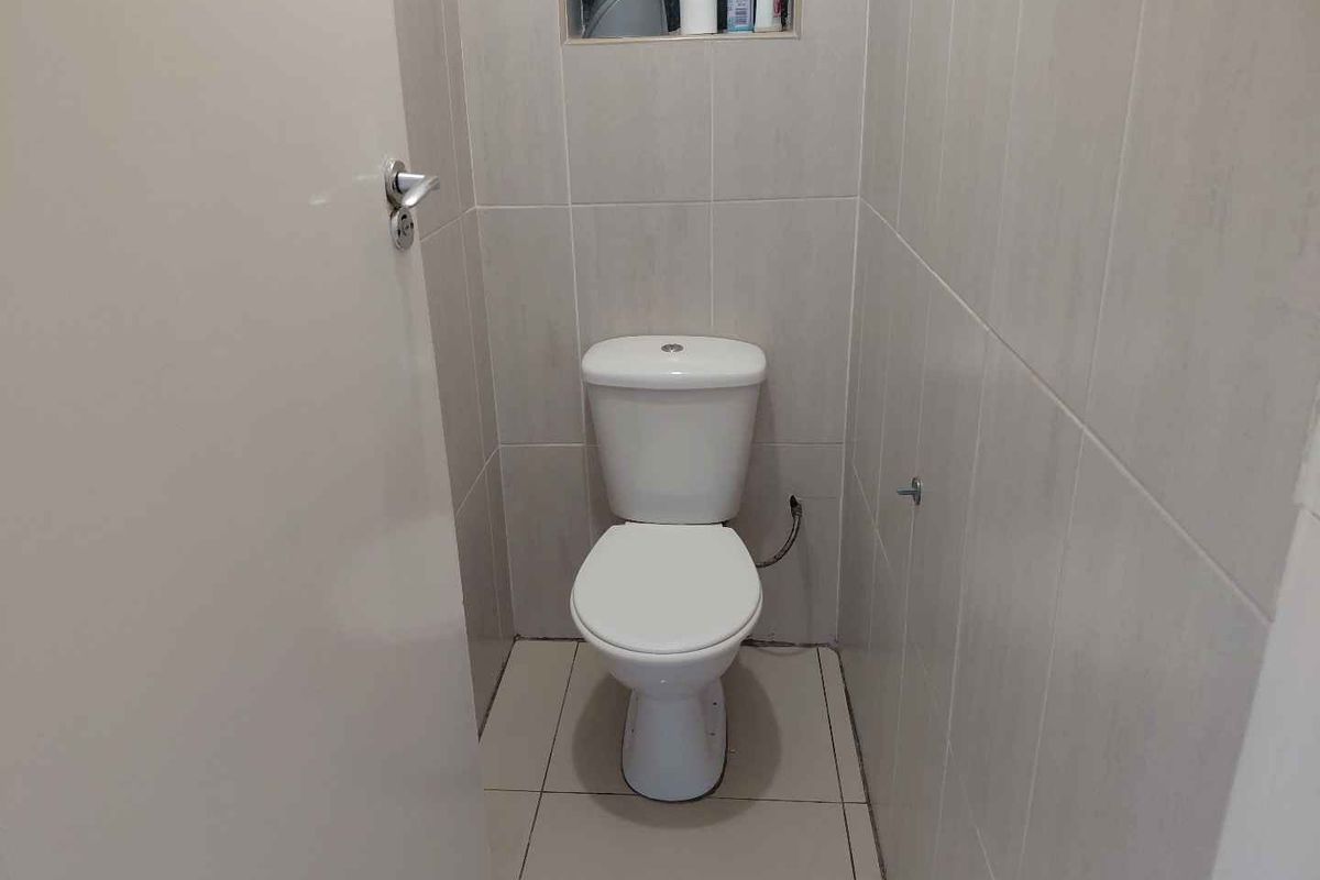 A compact, tiled guest toilet featuring neutral wall and floor finishes with a small high-level window for ventilation.