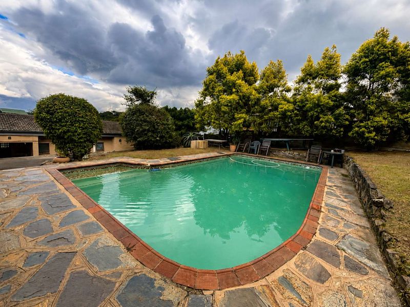 Outdoor pool area featuring a swimming pool with stone paving, brick coping, and a surrounding garden with mature trees.