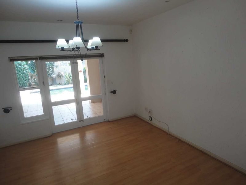 An empty living room featuring laminate flooring, a central chandelier, and double glass doors providing access to the outdoor patio and pool area.