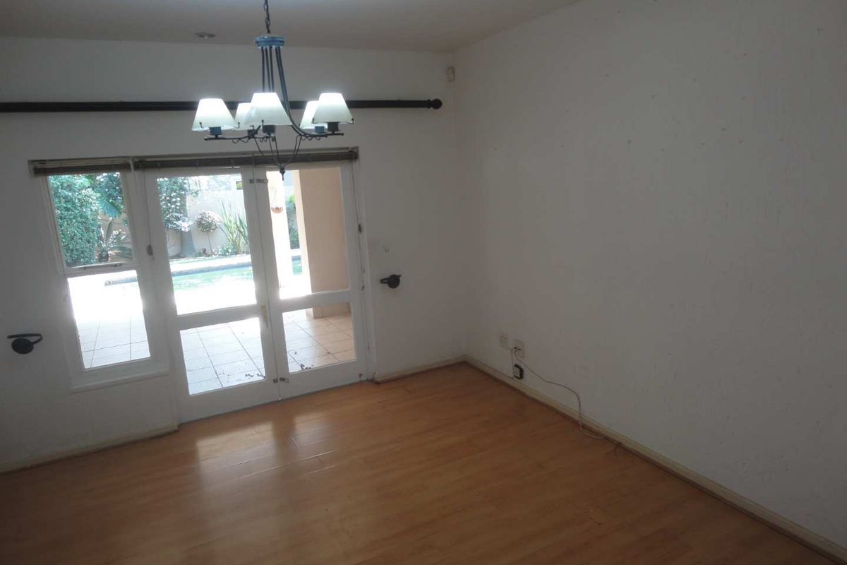 An empty living room featuring laminate flooring, a central chandelier, and double glass doors providing access to the outdoor patio and pool area.