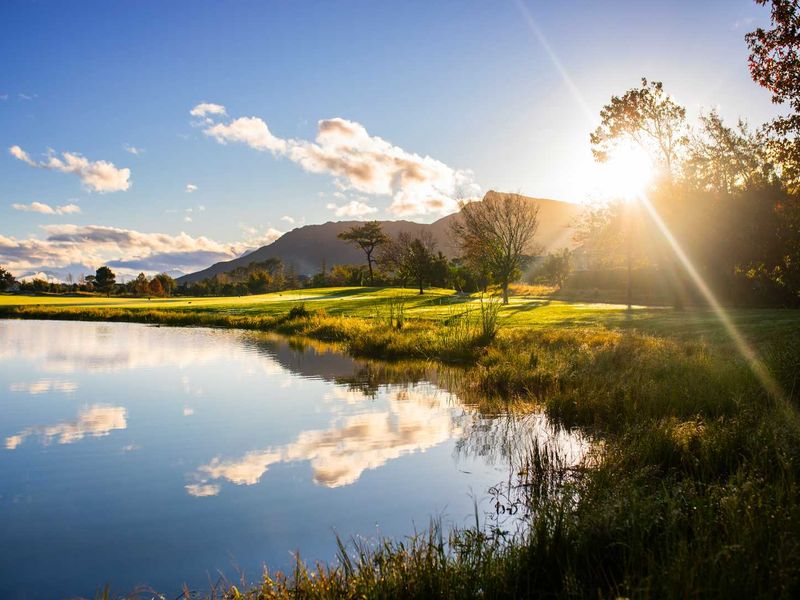 A scenic view of a tranquil lake with a golf course and mountain range in the background during sunset.