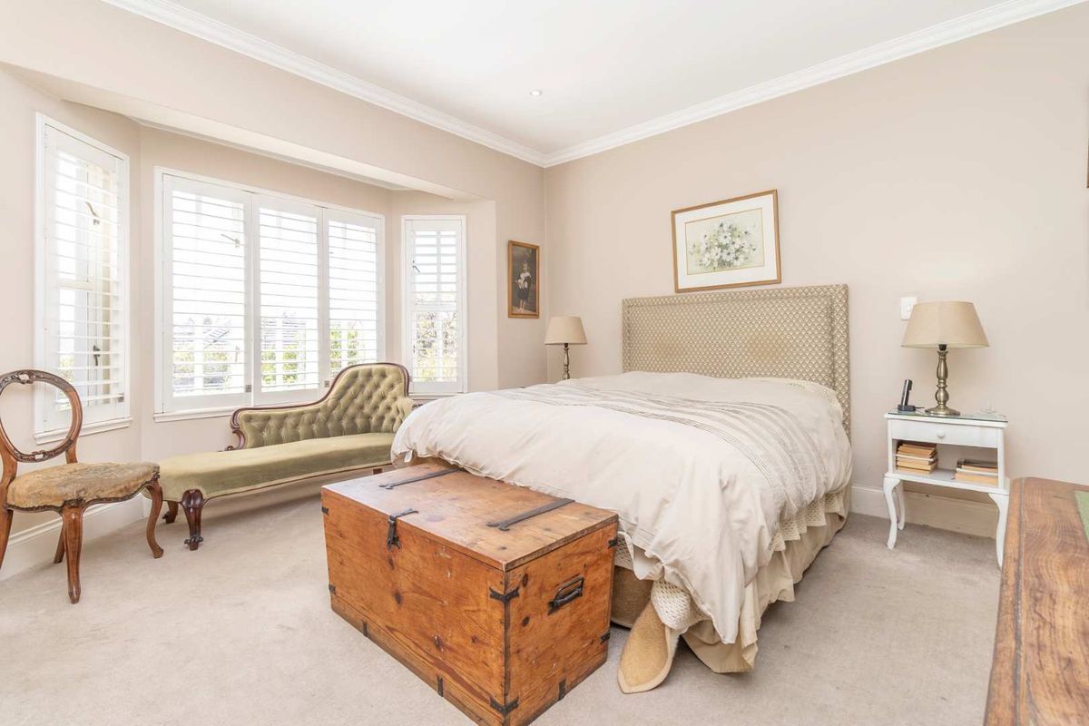 A well-maintained bedroom featuring neutral wall tones, plush carpeting, elegant cornicing, and plantation shutters that allow for adjustable natural light.