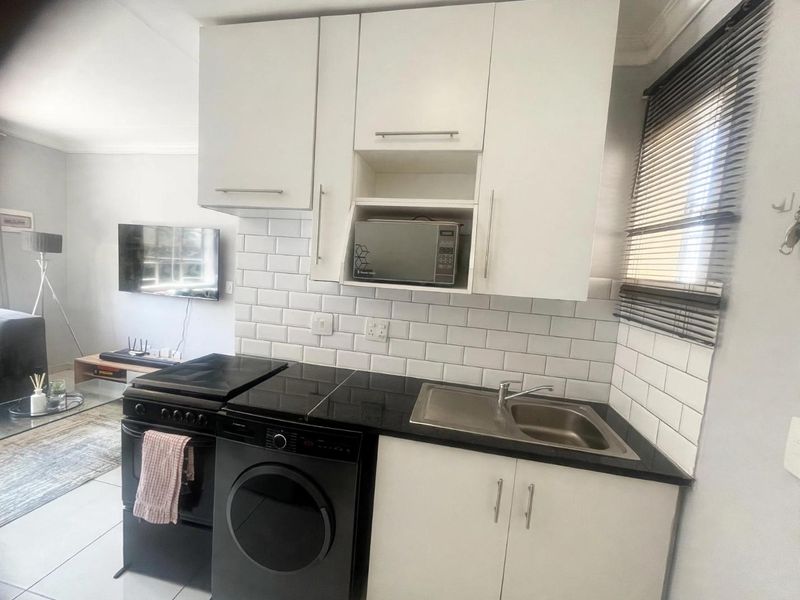 Compact kitchen featuring white cabinetry, black granite countertops, subway tile backsplash, and integrated microwave shelf, seamlessly connected to the living area.