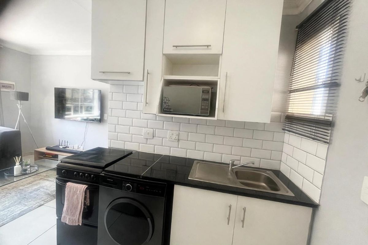 Compact kitchen featuring white cabinetry, black granite countertops, subway tile backsplash, and integrated microwave shelf, seamlessly connected to the living area.