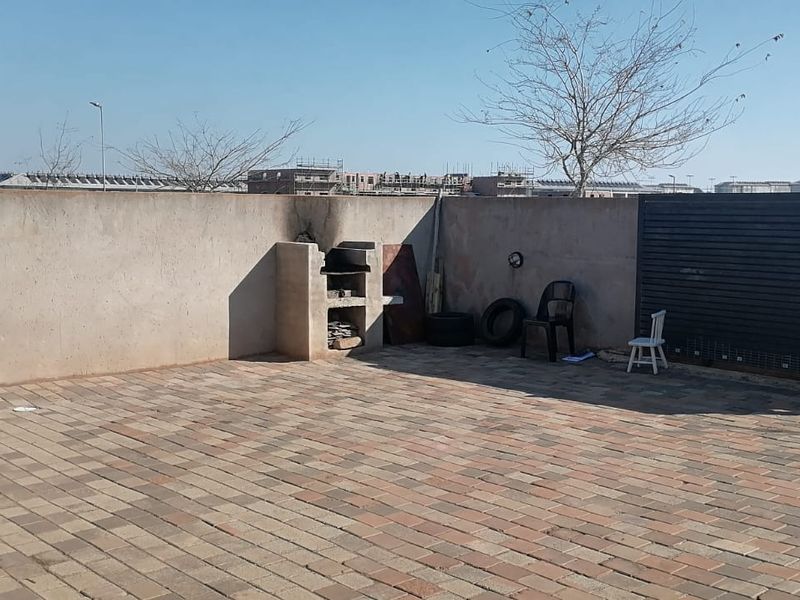 A paved outdoor patio area featuring a built-in braai and enclosed by boundary walls and a metal gate.