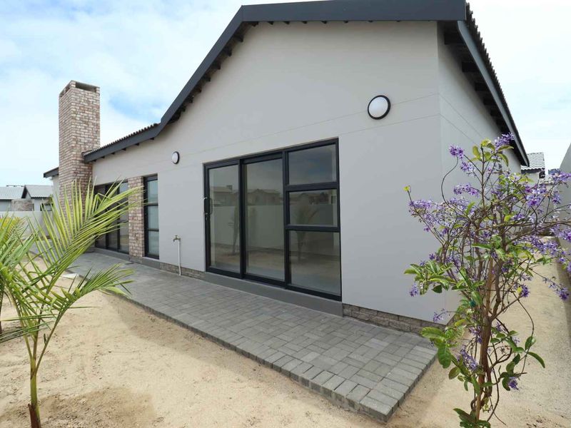 Rear view of the house featuring a paved patio, sliding glass doors, and a brick chimney, set against a landscaped garden area.