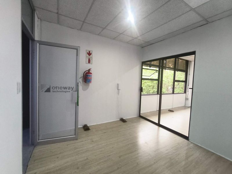 A bright, empty office space featuring laminate flooring, a suspended ceiling, and a glass sliding partition providing natural light and views.