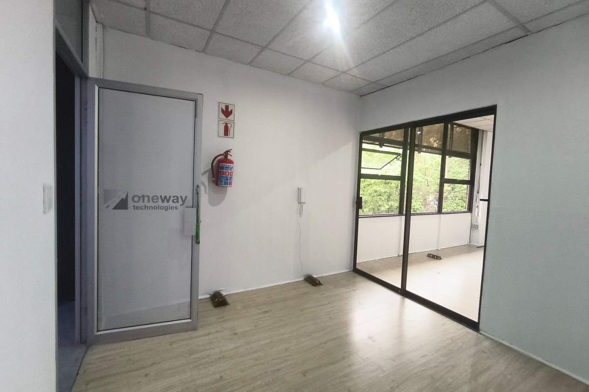 A bright, empty office space featuring laminate flooring, a suspended ceiling, and a glass sliding partition providing natural light and views.