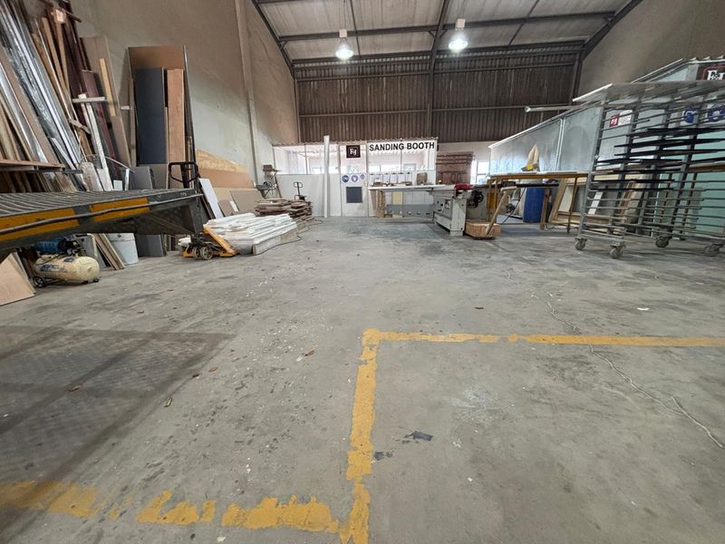 Industrial workshop space featuring concrete flooring, high-bay lighting, and a dedicated sanding booth enclosure within a steel portal frame structure.