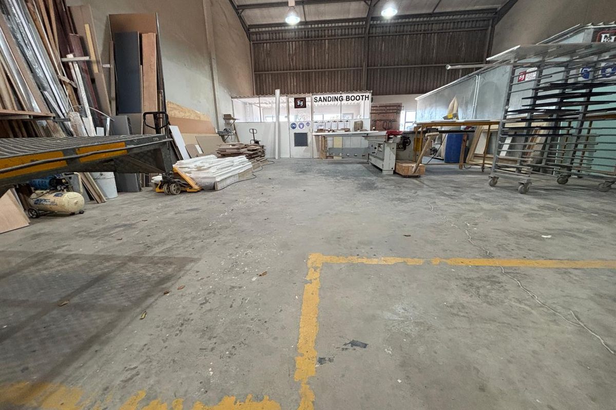 Industrial workshop space featuring concrete flooring, high-bay lighting, and a dedicated sanding booth enclosure within a steel portal frame structure.