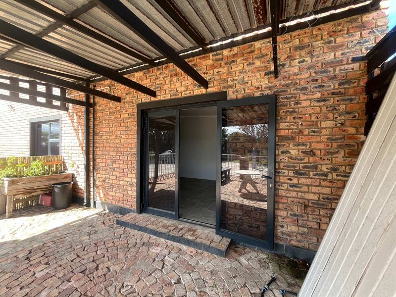 Covered outdoor patio area featuring exposed brick walls, corrugated metal roofing, and sliding glass doors leading into the interior space.
