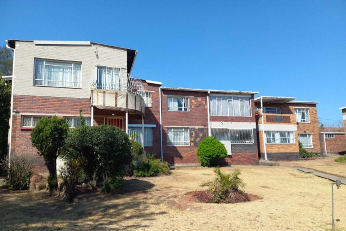 Exterior view of a multi-level townhouse complex featuring face-brick facade, security bars on windows, and a shared garden area.