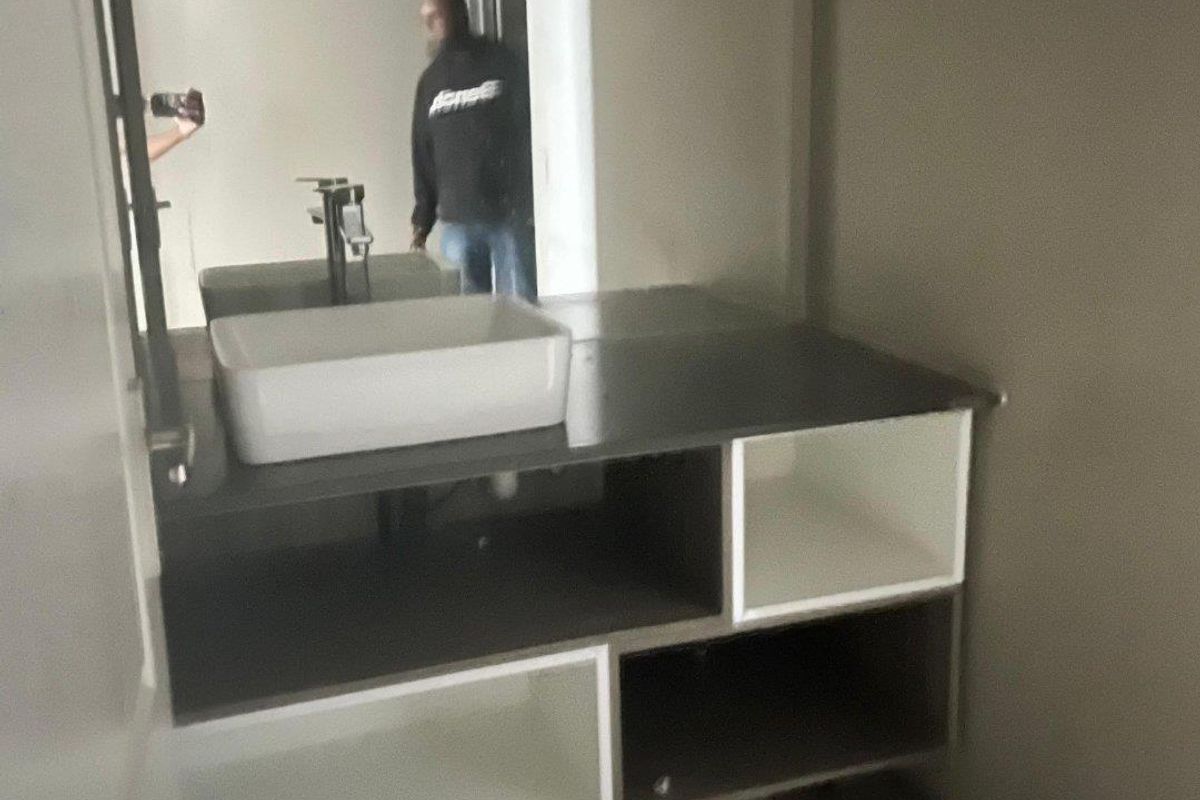 A modern bathroom vanity featuring a vessel sink, sleek faucet, and integrated storage shelving with a large wall-mounted mirror.