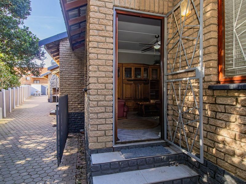Rear exterior view featuring a brick facade, paved walkway, security gate, and a built-in braai area along the side of the property.