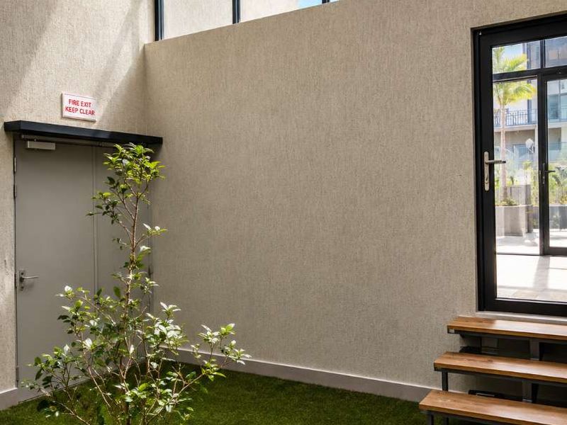 A modern, bright outdoor patio area featuring artificial turf, timber stairs, and large glass doors providing natural light and access.