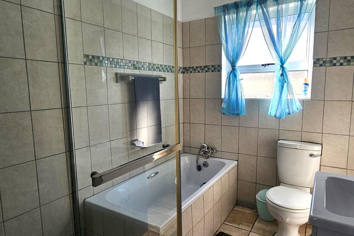 A functional bathroom featuring a tiled bathtub with a glass shower screen, a standard toilet, and neutral wall tiling.