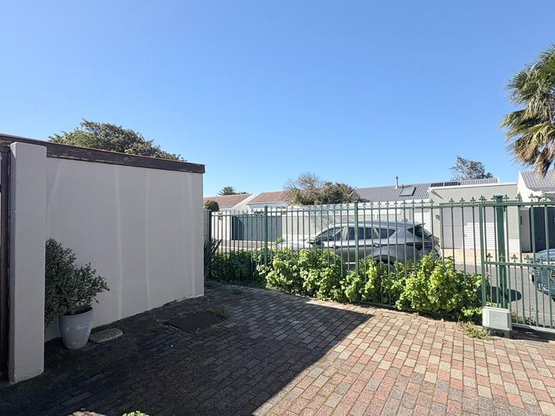 A paved rear courtyard area featuring secure metal fencing, a gated entrance, and a solid boundary wall.