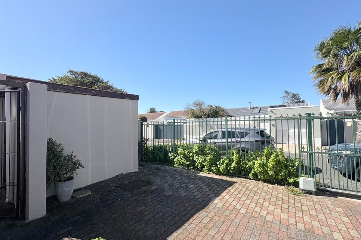 A paved rear courtyard area featuring secure metal fencing, a gated entrance, and a solid boundary wall.