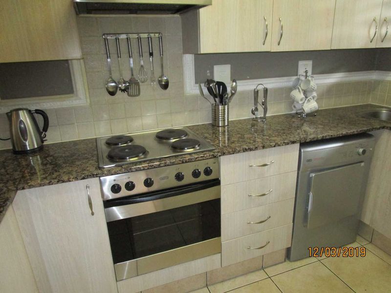 A functional kitchen featuring granite countertops, light wood-finish cabinetry, a built-in oven with electric hob, and a tiled backsplash.