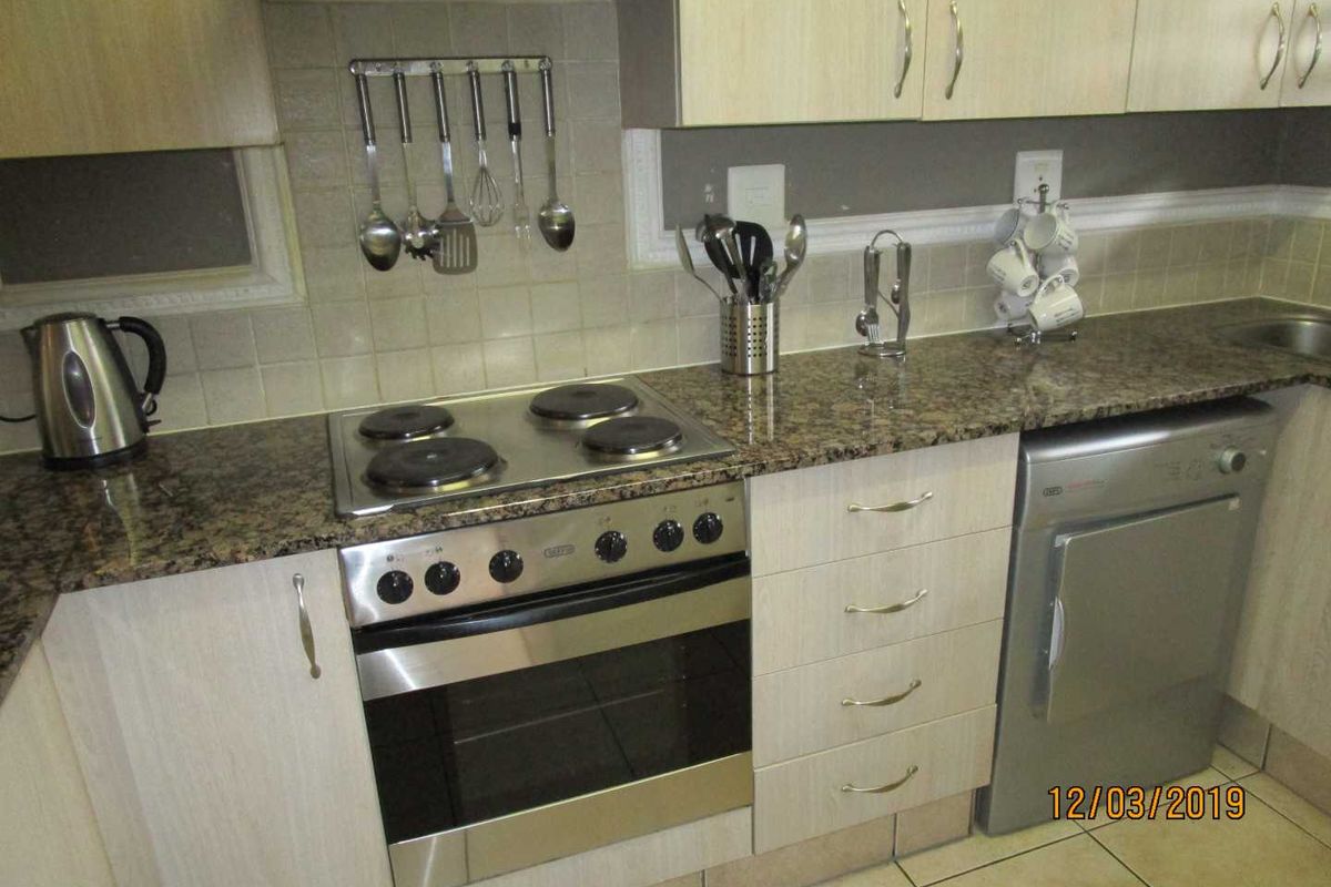 A functional kitchen featuring granite countertops, light wood-finish cabinetry, a built-in oven with electric hob, and a tiled backsplash.