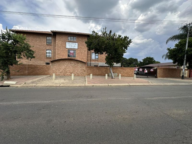 Street-facing view of Hieswil Villa apartment complex, featuring a brick facade, perimeter wall, and secure gated entrance.