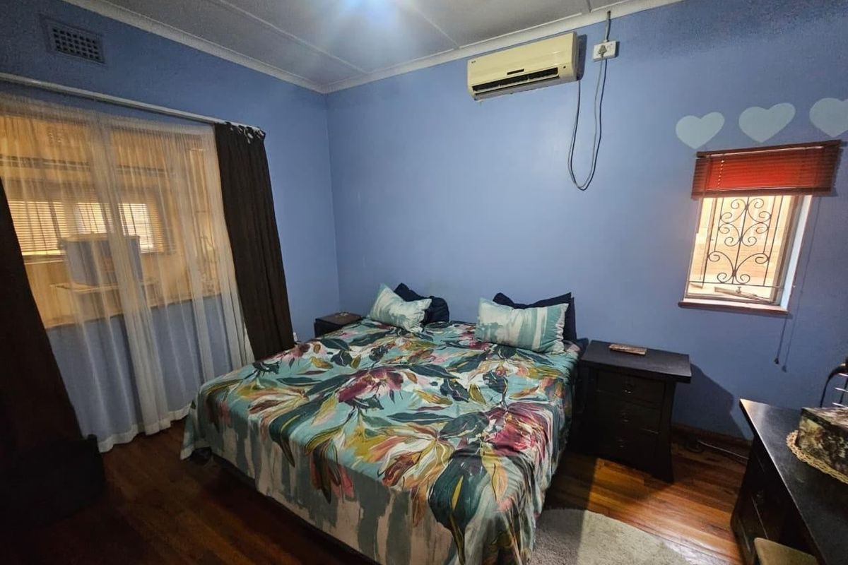 A bedroom featuring hardwood flooring, a wall-mounted air conditioning unit, and security bars on the window.