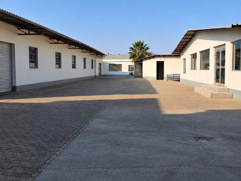 A view of the industrial property's rear courtyard featuring paved surfaces, multiple building access points, and industrial roller shutter doors.