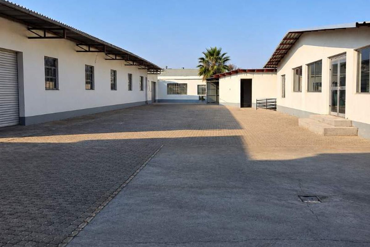 A view of the industrial property's rear courtyard featuring paved surfaces, multiple building access points, and industrial roller shutter doors.